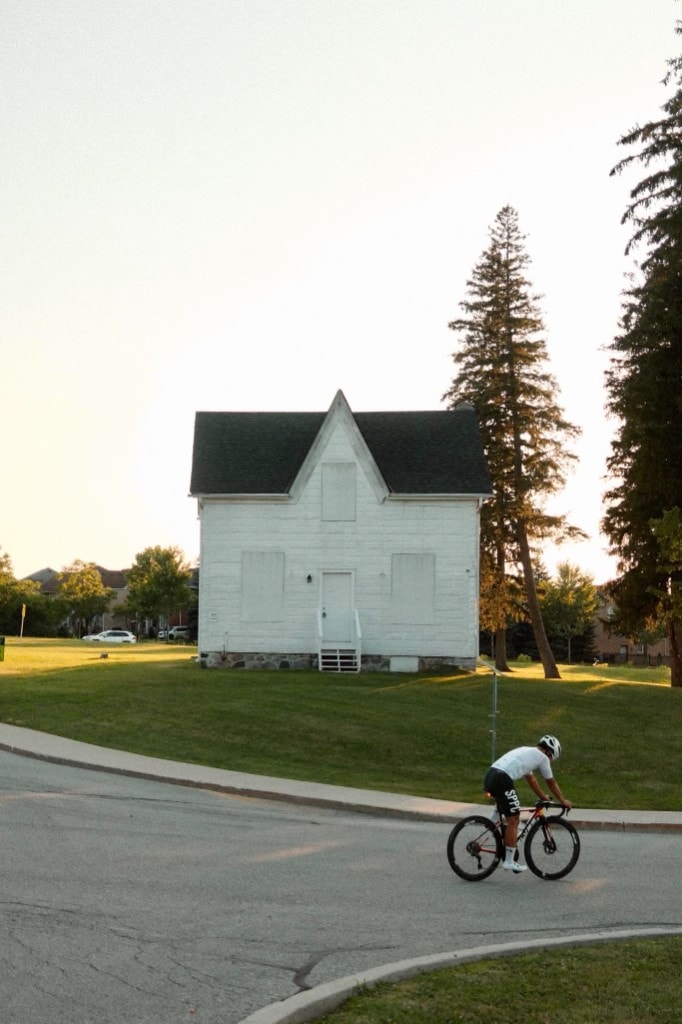 A rider rolling past a white clapboard house at golden hour